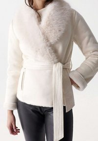 Cremefarbene Wickeljacke mit einem Kragen und Manschetten aus Kunstpelz, tailliert mit Gürtel und strukturierter Stoff. Verfügt über seitliche Reißverschlusstaschen und gerippte Akzente.