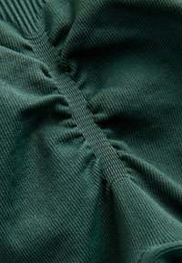 Tume roheline kangas soonilise tekstuuriga, millel on kogutud lõigud ja sile õmblus, mis kulgeb vertikaalselt keskel.