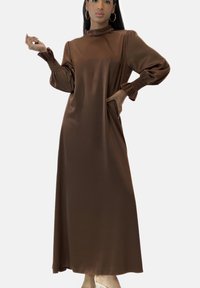 Braunes Satinkleid in Maxilänge mit hohem Ausschnitt und Puffärmeln, mit gerafften Handgelenkdetails und seitlichen Taschen. Glatte, glänzende Textur.