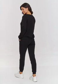 Czarny zestaw bluz i spodni dresowych o luźnym kroju. Materiał bawełniany, ściągacze na mankietach, kieszenie boczne, zestawiony z białymi trampkami.