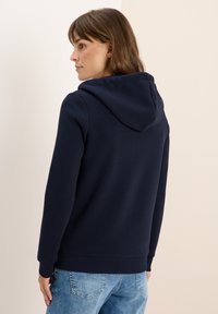 Sweatshirt à capuche bleu marine avec une finition texturée, poignets et ourlet côtelés, présentant une coupe décontractée, associé à un jean en denim bleu clair.