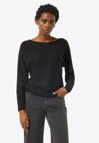 Schwarzer Pullover mit langen Ärmeln und weitem Ausschnitt, aus einem weichen Material, kombiniert mit dunkelgrauen Jeans. Der Stoff wirkt glatt und leicht.