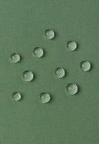 Tessuto verde testurizzato con diverse gocce d'acqua trasparenti appoggiate sulla superficie, che evidenziano le sue proprietà resistenti all'acqua.