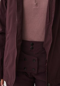 Bordeaux jack met ritssluiting aan de voorkant en een fleece binnenkant, gecombineerd met bijpassende bordeaux broek met zwarte drukknoopjes en zakken.