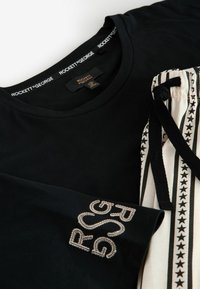 Czarna bawełniana koszulka z haftowanym napisem "RSG" oraz białe spodnie ze ściągaczem, ozdobione czarnym wzorem gwiazdek i sznurkiem.