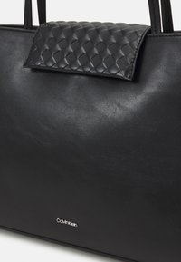 Borsa tote in pelle nera con patta trapuntata, texture liscia e discreto logo Calvin Klein in argento sul fronte.