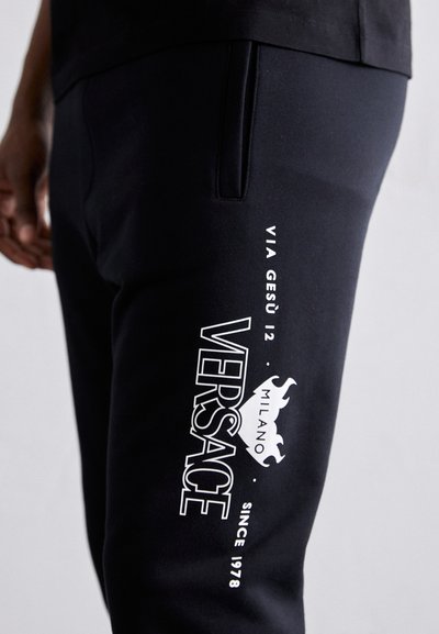 Mustad mustad, millel on valge bränding, sealhulgas "VERSACE", "MILANO" ja logo, sujuvast kangast ja uhkest lõikest.