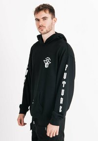 Schwarzes Kapuzensweatshirt mit einer Fronttasche, featuring weiße Grafiken auf der Brust und den Ärmeln, im lässigen Schnitt. Weicher Stoff, lange Ärmel.