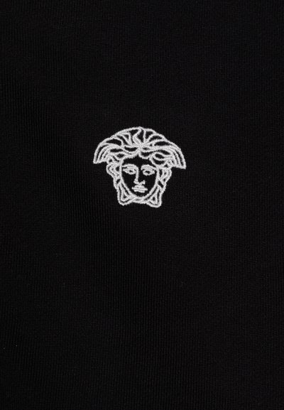 Black fabric with a textured finish featuring a white embroidered logo of a face with wavy hair at the center.