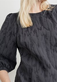 Blusa nera con texture e maniche voluminose, caratterizzata da un motivo sottile e un collo rotondo. Tessuto leggero con una finitura morbida.