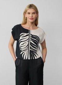 Blouse noir et blanc avec un grand imprimé de feuilles, manches courtes et col rond, fabriquée dans un tissu lisse et léger.