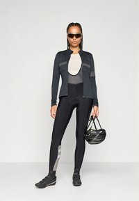 Strój kolarski składający się z czarnej długorękawowej koszulki i dopasowanych czarnych legginsów z szarymi akcentami, uzupełniony butami kolarskimi i kaskiem.