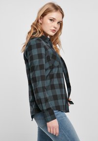 Schwarz und türkis kariertes Flanellhemd mit langen Ärmeln, Kragen, Tasche auf der Vorderseite und abgerundetem Saum, kombiniert mit hellblauen Jeans.