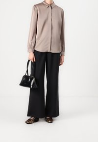 Satinbrun blus med puffärmar, i kombination med lösa svarta byxor och läppardoftande ballerinaskor. Håller en liten svart handväska.