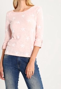Ljusrosa långärmad topp med vita sjöstjärnemönster, rundad halsringning och rullade ärmar. Matchas med blå jeans.