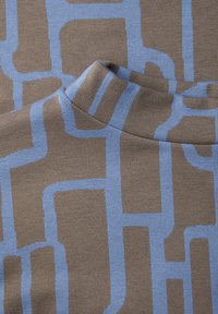 Tela de punto marrón con un patrón geométrico azul y textura suave. El diseño incluye varias formas y líneas interconectadas.