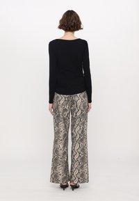 Zwarte lange mouwen top met een ronde hals, gecombineerd met wijde broek met een beige en zwart slangprintpatroon.