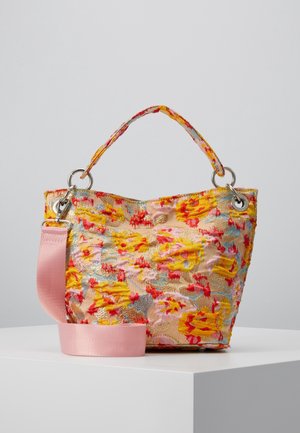 Petit sac fourre-tout avec tissu texturé floral jaune, rouge et rose, poignée courte et large sangle d'épaule rose amovible sur un piédestal blanc.