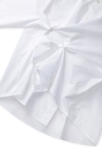 White long-sleeve shirt made of cotton. Features buttons down the front, a twist detail at the waist, and a curved hem. Plain texture.