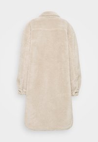 Béžová fleecová svrchní bunda, dlouhá s límcem, s měkkou texturou, zaobleným lemem a staženými elastickými manžetami. Zobrazen pohled zezadu.