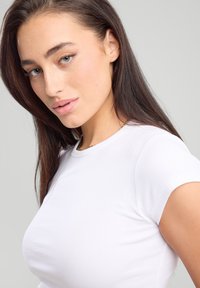 T-shirt bianco a coste con maniche corte, caratterizzata da un collo a giro. Il tessuto appare liscio e leggermente testurizzato. Il modello assume una posa naturale.