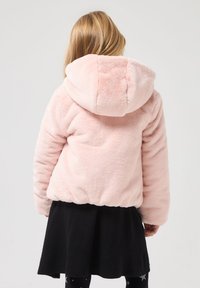 Felpa rosa pelosa con cappuccio arrotondato, texture morbida e orlo arricciato. Abbinata a una gonna nera con design svasato.
