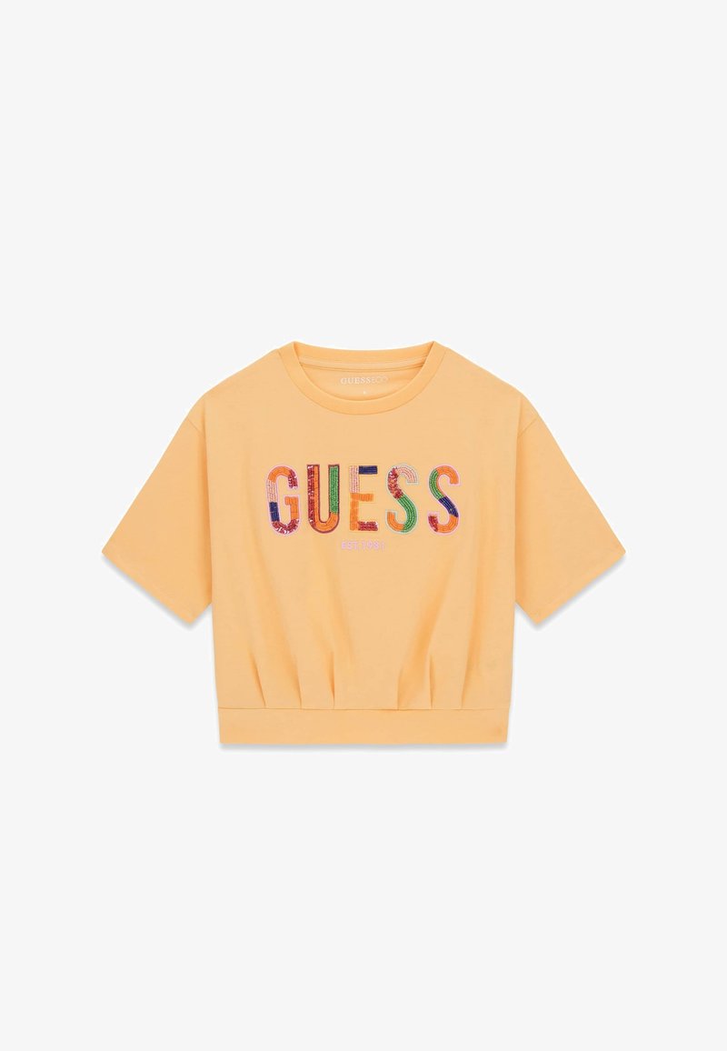 Kurzes, pfirsichfarbenes, bauchfreies T-Shirt mit mehrfarbigem "GUESS"-Schriftzug und der Aufschrift "EST. 1981" auf der Vorderseite.