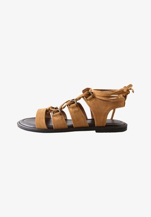 Sandale gladiator din piele întoarsă maro, cu talpă plată neagră și mai multe barete șnuruite prin inele metalice, legate la spatele gleznei.