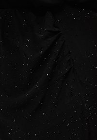 Sort stoff med en teksturert overflate, med spredte små klare paljetter som reflekterer lys og skaper en glitrende effekt.