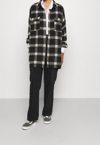 Person wearing black and white plaid button-up shirt, white shirt underneath, black cargo pants, and green sneakers with white laces.