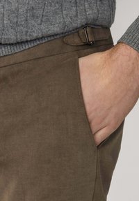 Brązowe spodnie z korduroyu o gładkiej fakturze, z boczną kieszenią i paskiem z ciemnym metalowym klamrą.