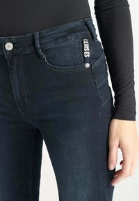 Donkerblauwe denim jeans met een klassiek ontwerp, vijf zakken, gestikte details en een logo accent op de tailleband.