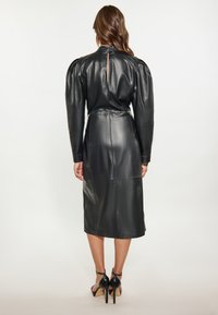 Schwarzes Lederkleid mit langen Puffärmeln und tailliertem Schnitt, ausgestattet mit einem Reißverschluss auf der Rückseite und einem knielangen Saum. Glatte Textur und strukturierte Form.