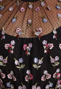 Robe en maille noire ornée de broderies florales en rose, bleu clair et vert. Présente des accents en sequins sur les fleurs et un tissu texturé.