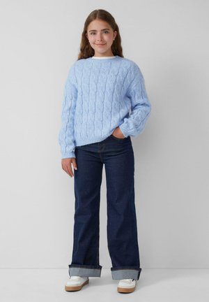 Lichtblauwe, kabelgebreide trui met een comfortabele pasvorm. Gecombineerd met donkerdenim wijde jeans met opgerolde boorden en witte sneakers.
