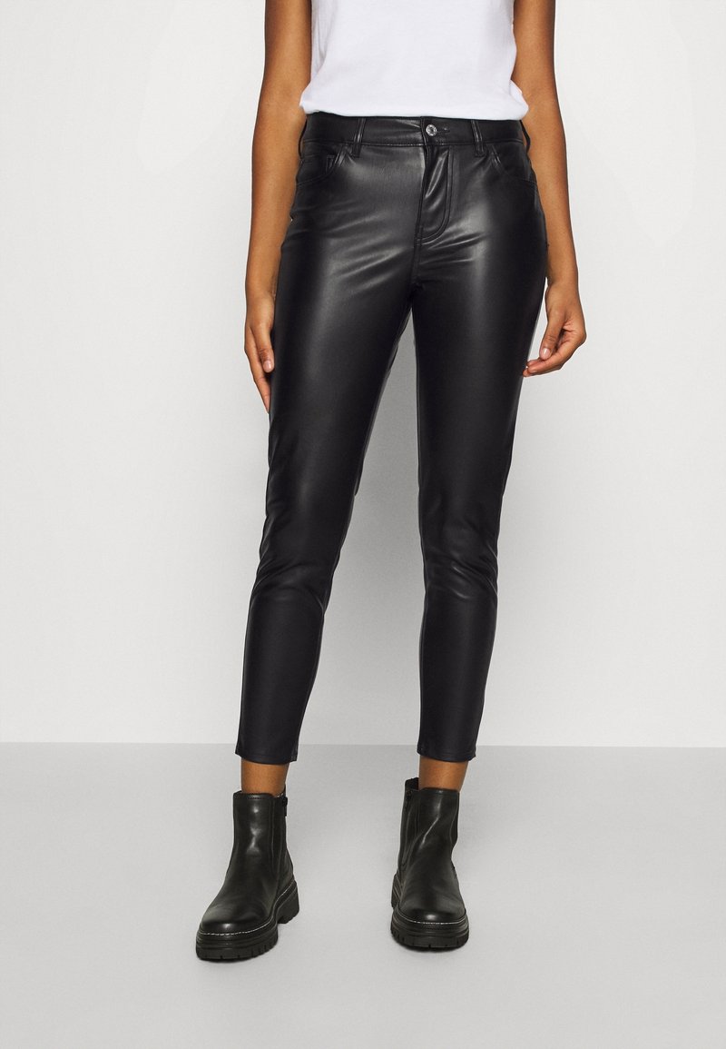 Black faux leather skinny pants with a high waist, featuring front pockets and a smooth texture, paired with chunky black ankle boots.