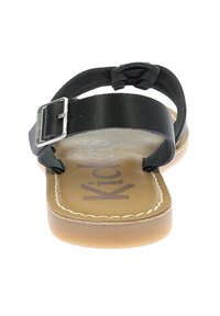 Sandalias de cuero negro con una correa con hebilla, plantilla de color tostado, costuras en contraste y una suela plana de goma. El texto dice "Niño."