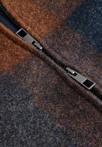 Wool zip-up fabric with a blend of brown, grey, and navy blue colors. Features a metal zipper along the seam for closure.