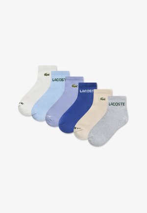 Zes paar Lacoste-sokken in verschillende pasteltinten: wit, lichtblauw, lavendel, blauw, beige en grijs. Elk paar heeft een logo en een contrasterende band.