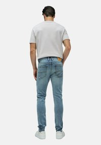 Zbledele modre jeans hruške z ožjim krojem, ki imajo usnjeni pečat na zadnjem delu pasu in dva zadnja žepa. Uporabljeni so z svetlo sivo majico.
