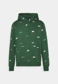 Grön hooded sweatshirt med en framficka, prydd med vita Nike-loggor och textmönster genom hela tyget. Mjuk, avslappnad design.