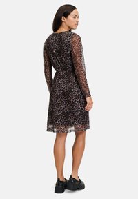 Langärmliges Kleid mit Tierdruck aus transparentem Stoff mit taillierter Passform. Es hat einen runden Ausschnitt und endet knapp über dem Knie, kombiniert mit schwarzen Plateauschuhen.