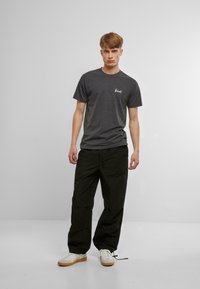 Grau meliertes Baumwoll-T-Shirt mit kurzen Ärmeln, versehen mit einem kleinen weißen Grafik auf der Brust, kombiniert mit schwarzen lockeren Hosen und weißen Turnschuhen.