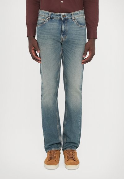 Blue denim jeans with a faded wash, straight leg design, five pockets, and a button closure. Paired with brown suede sneakers.