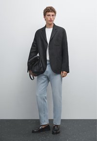 Black blazer with a single pocket, white T-shirt, light blue jeans, black loafers, and holding a black leather bag. Smooth, tailored fit.