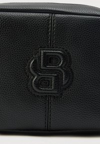 Čierne kožené kozmetické puzdro s textúrovaným povrchom a razeným logom, ktoré sa vyznačuje minimalistickým dizajnom a jemnými švami.