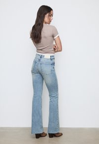 Jeans svasati azzurro chiaro con un orlo leggermente sfrangiato e due tasche posteriori, abbinati a un top aderente marrone con rifiniture bianche.