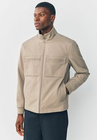 Lys beige zip-up jakke lavet af glat stof, med to brystlommer med lynlåslukninger og en stand-up krave.
