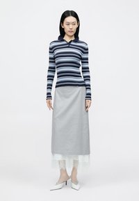 Tengerészkék és világoskék csíkos bordázott hosszú ujjú galléros póló, szürke midi szoknyával, amelyen csipkebetétes szegély található, fehér hegyes orrú cipőkkel párosítva.