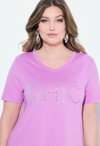 Lavender V-hals T-shirt med "CHIC" i rhinstenar. Korta ärmar, mjuk textur, avslappnad passform och subtil randig mönster.